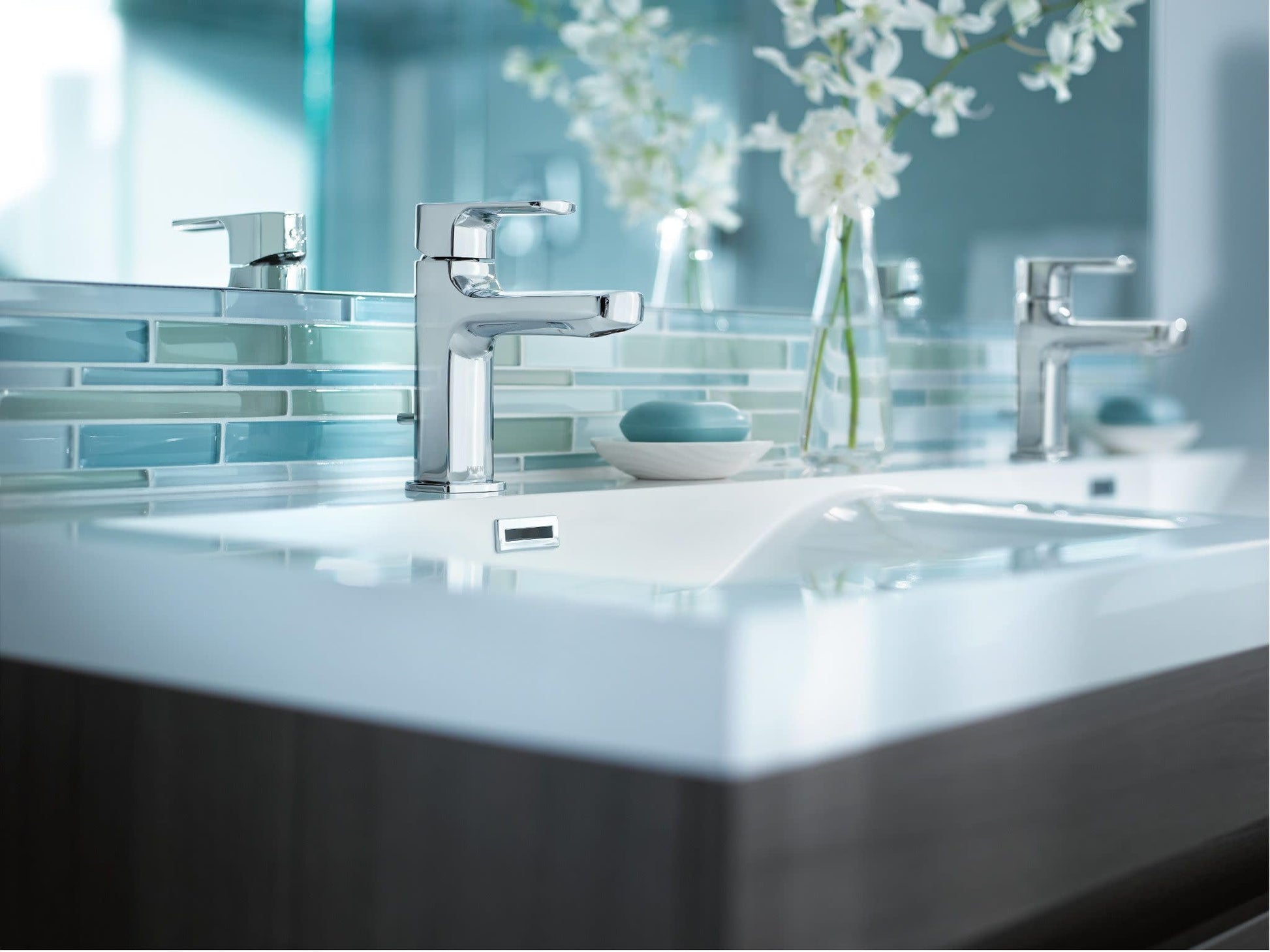 Chrome single-handle bathroom faucet with rectangular spout mounted on white sink countertop.