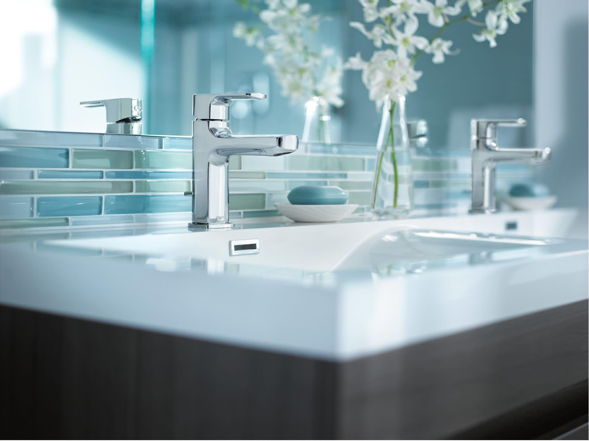 Chrome single-handle bathroom faucet with rectangular spout mounted on white sink countertop.