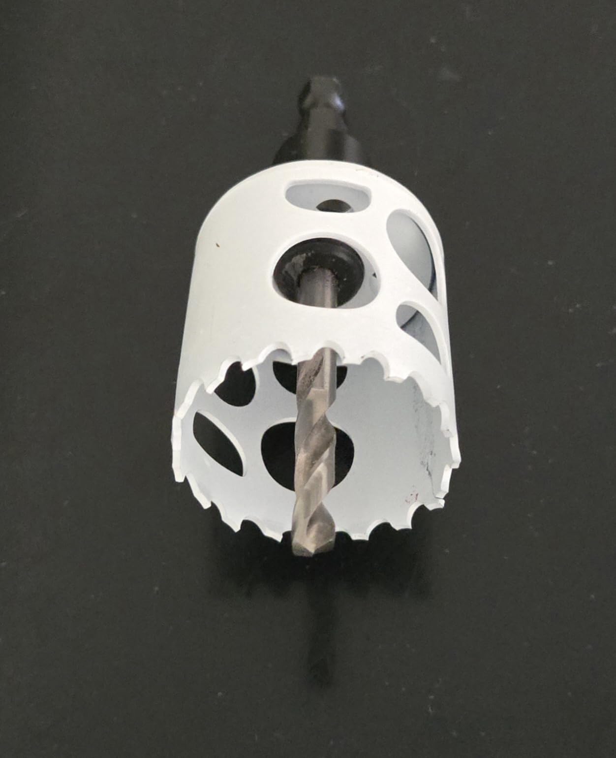 White bi-metal hole saw with serrated cutting edges and center arbor drill bit attached.