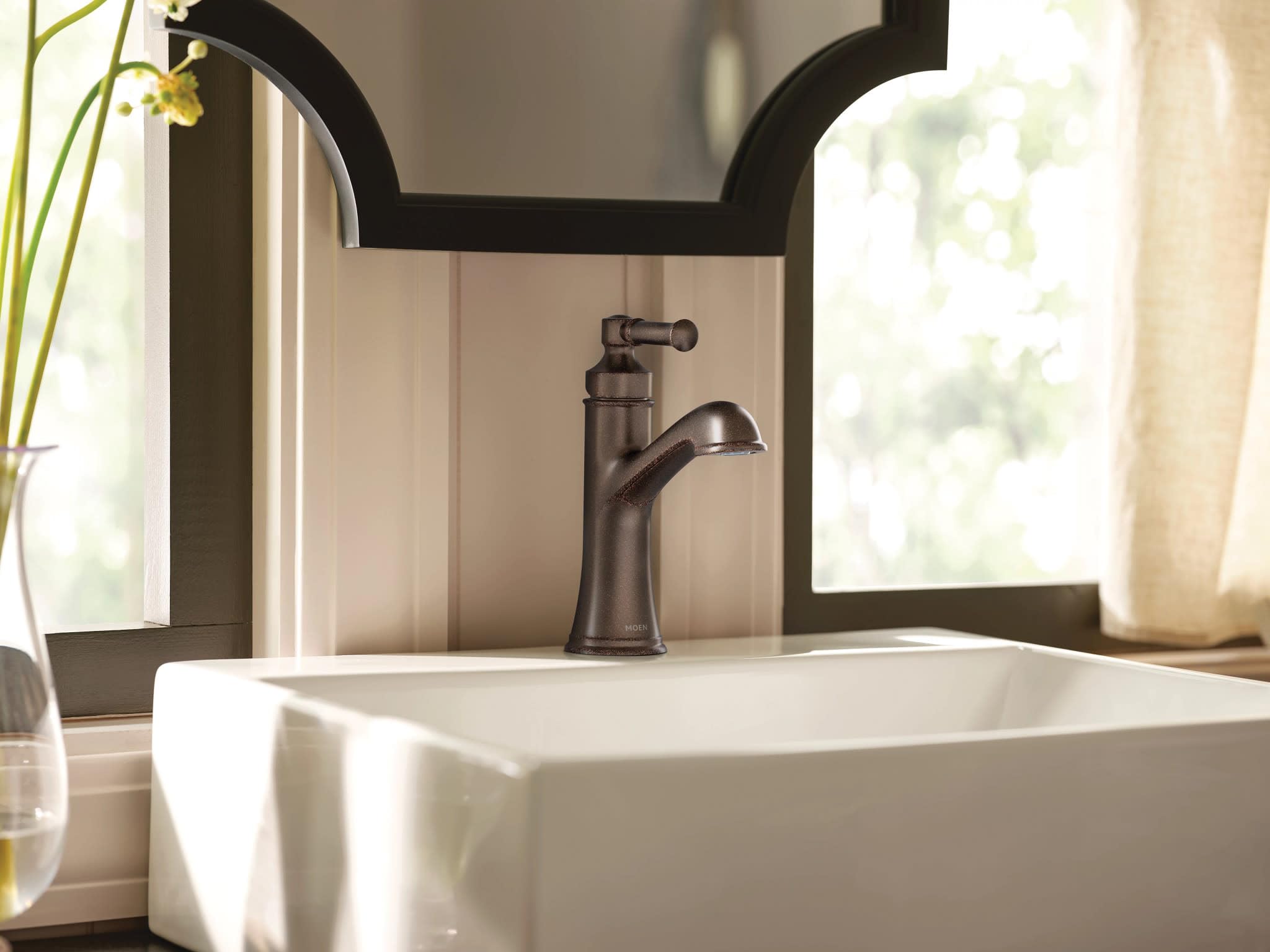 Oil rubbed bronze single-handle bathroom faucet with curved spout mounted on white vessel sink.