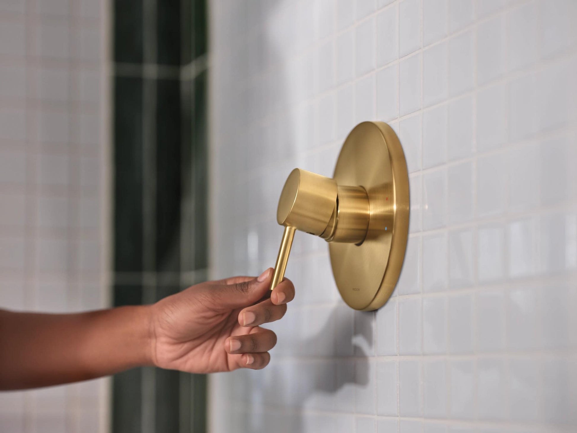 Brushed gold shower trim with lever handle and round escutcheon plate mounted on white tile wall.