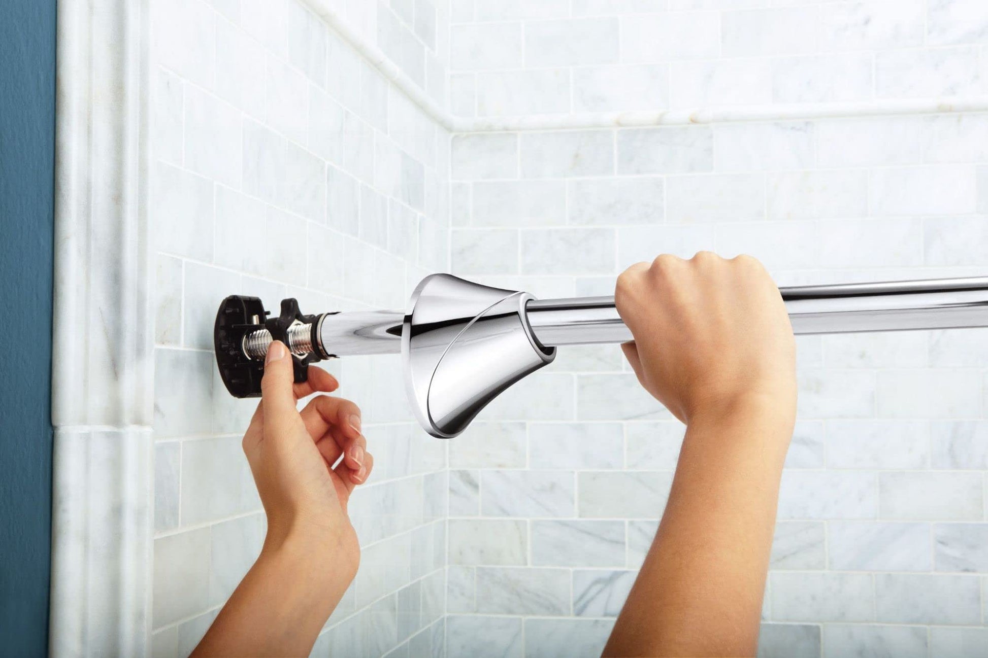 Chrome curved tension shower rod being installed between bathroom tile walls with mounting hardware visible.