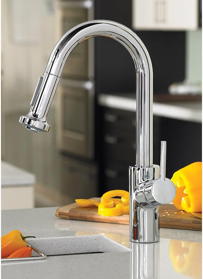Chrome kitchen faucet with curved spout and pull-down spray head positioned over sink counter with yellow peppers.