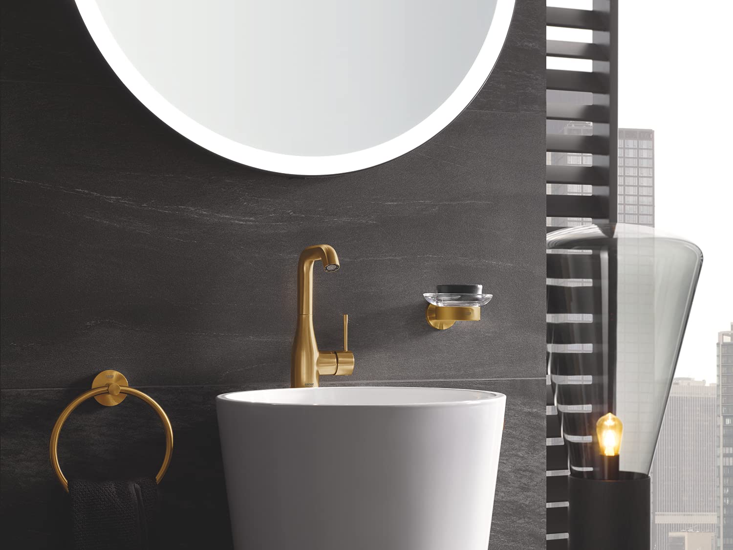 Brushed gold towel ring mounted on dark wall next to white basin and faucet.