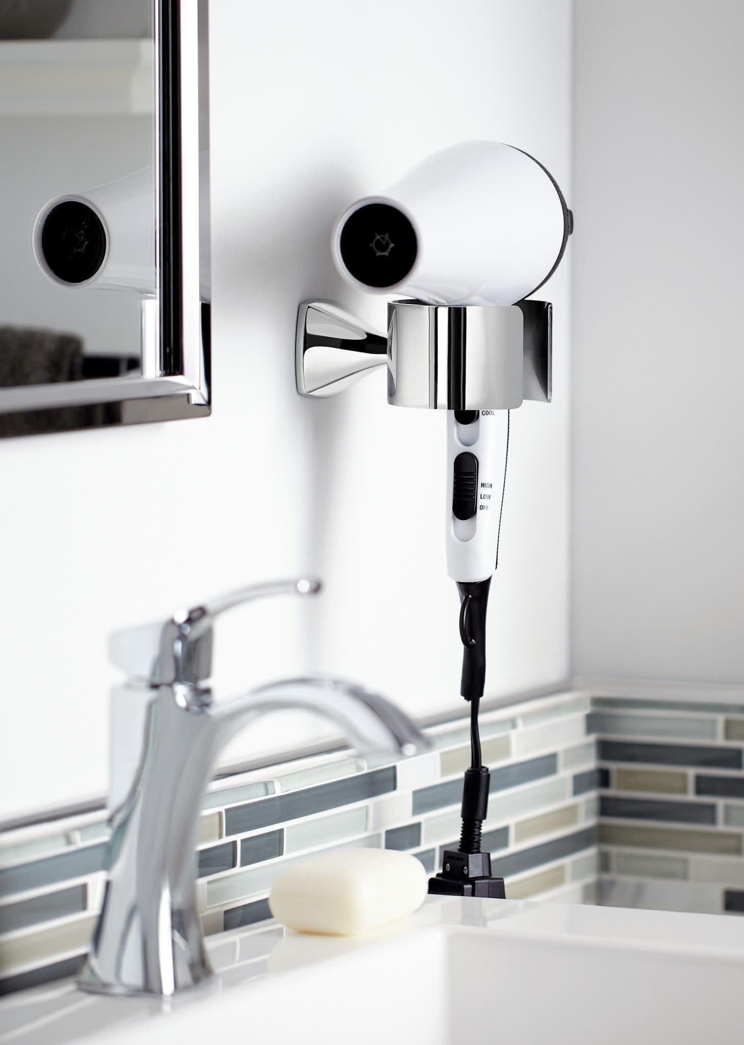Chrome single-handle bathroom sink faucet with cylindrical spout mounted on white wall above sink basin.