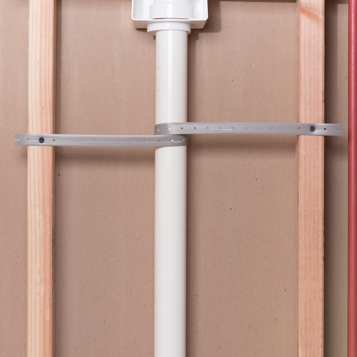 Two gray metal securing straps with mounting holes fastened horizontally around a white PVC pipe between wooden framing.