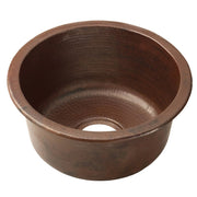 Hammered copper round bar sink with dark patina finish and drain opening.