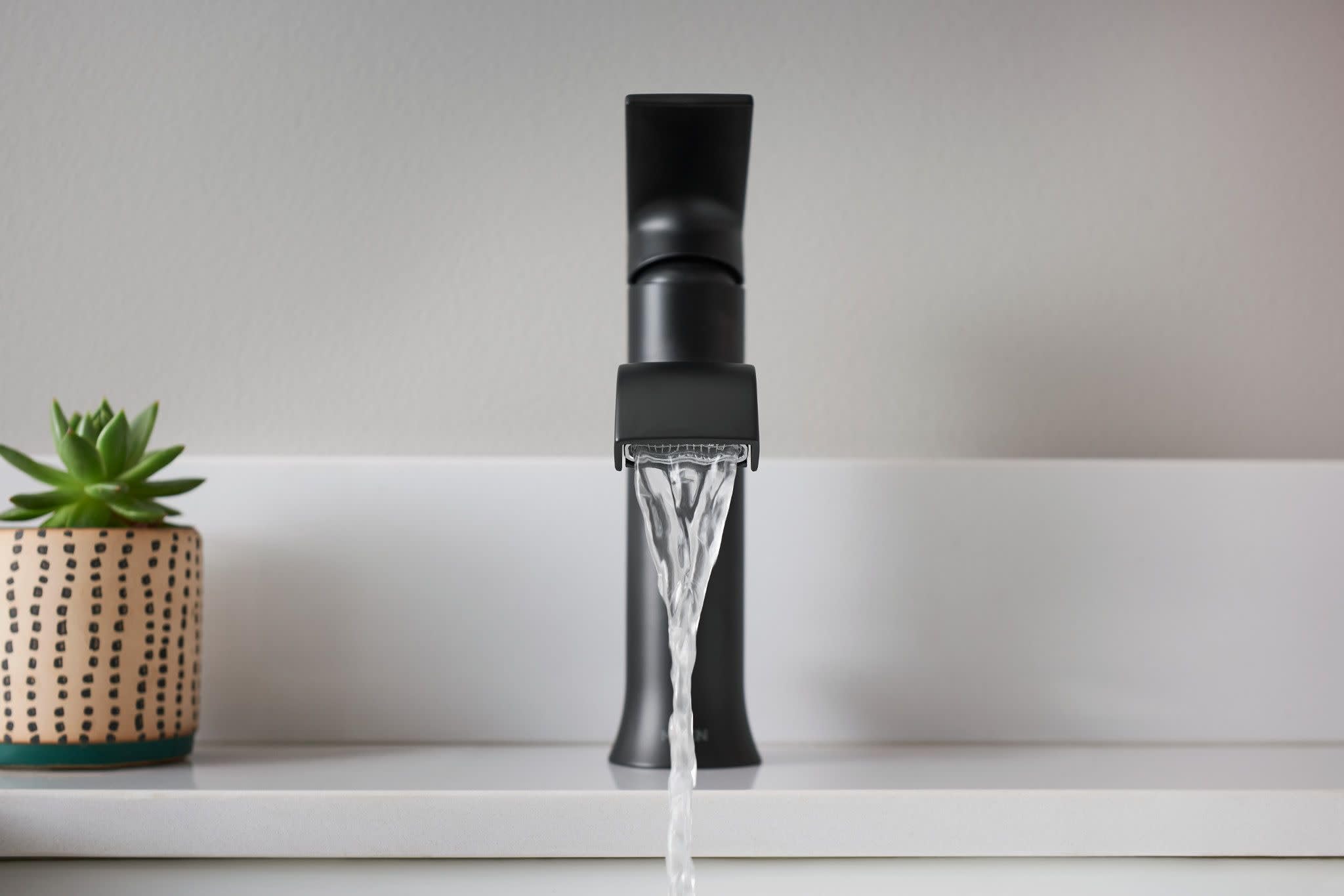Matte black single-handle bathroom faucet with tall spout dispensing water, displayed on white countertop.