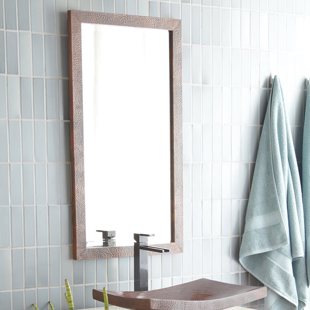 Rectangular mirror with textured antique frame mounted above bathroom sink with faucet and towels.