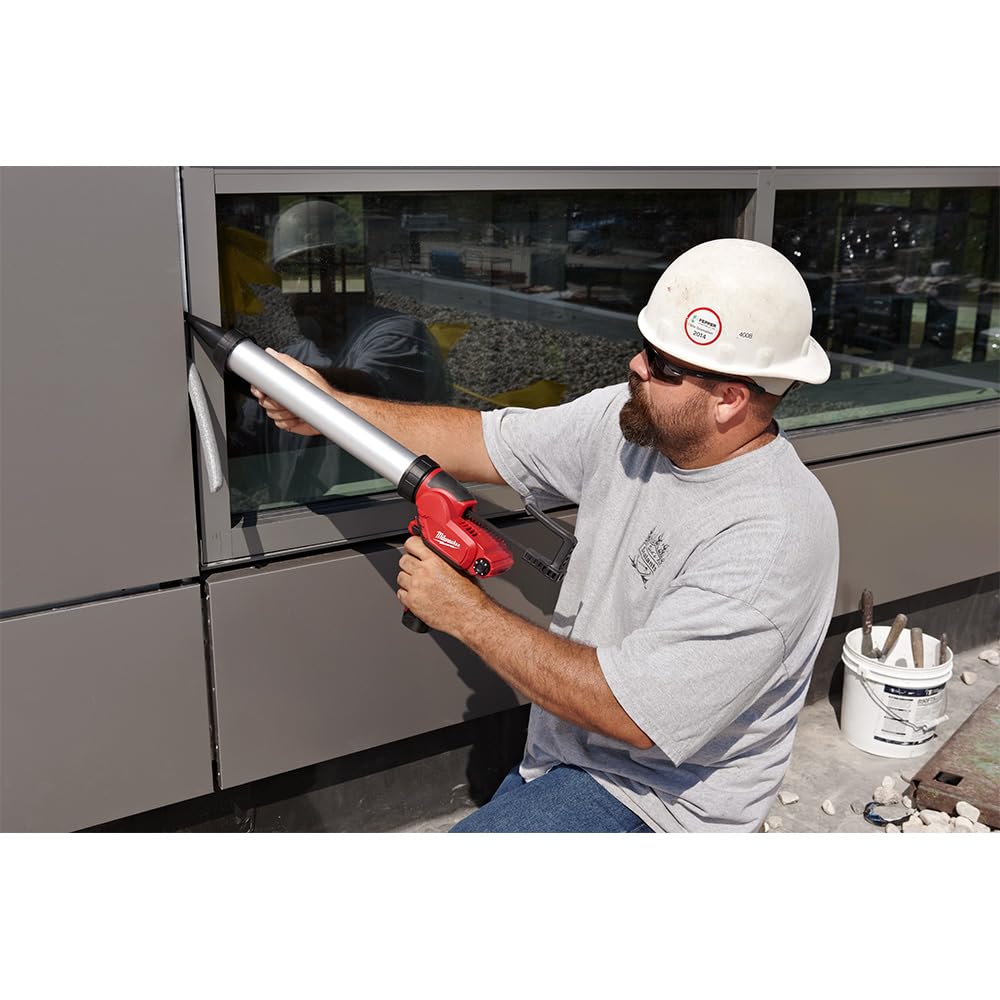 Worker in white hard hat using red and black Milwaukee caulk gun with silver barrel on building exterior.