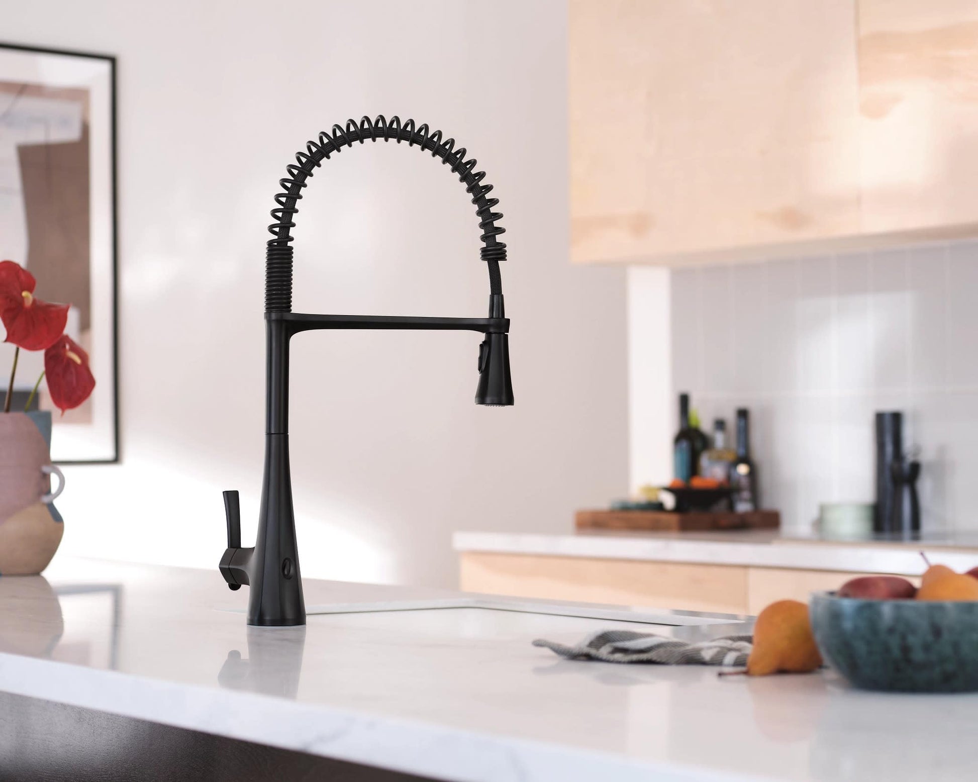 Matte black high arc kitchen faucet with coiled pulldown sprayer hose and single lever handle on white countertop.