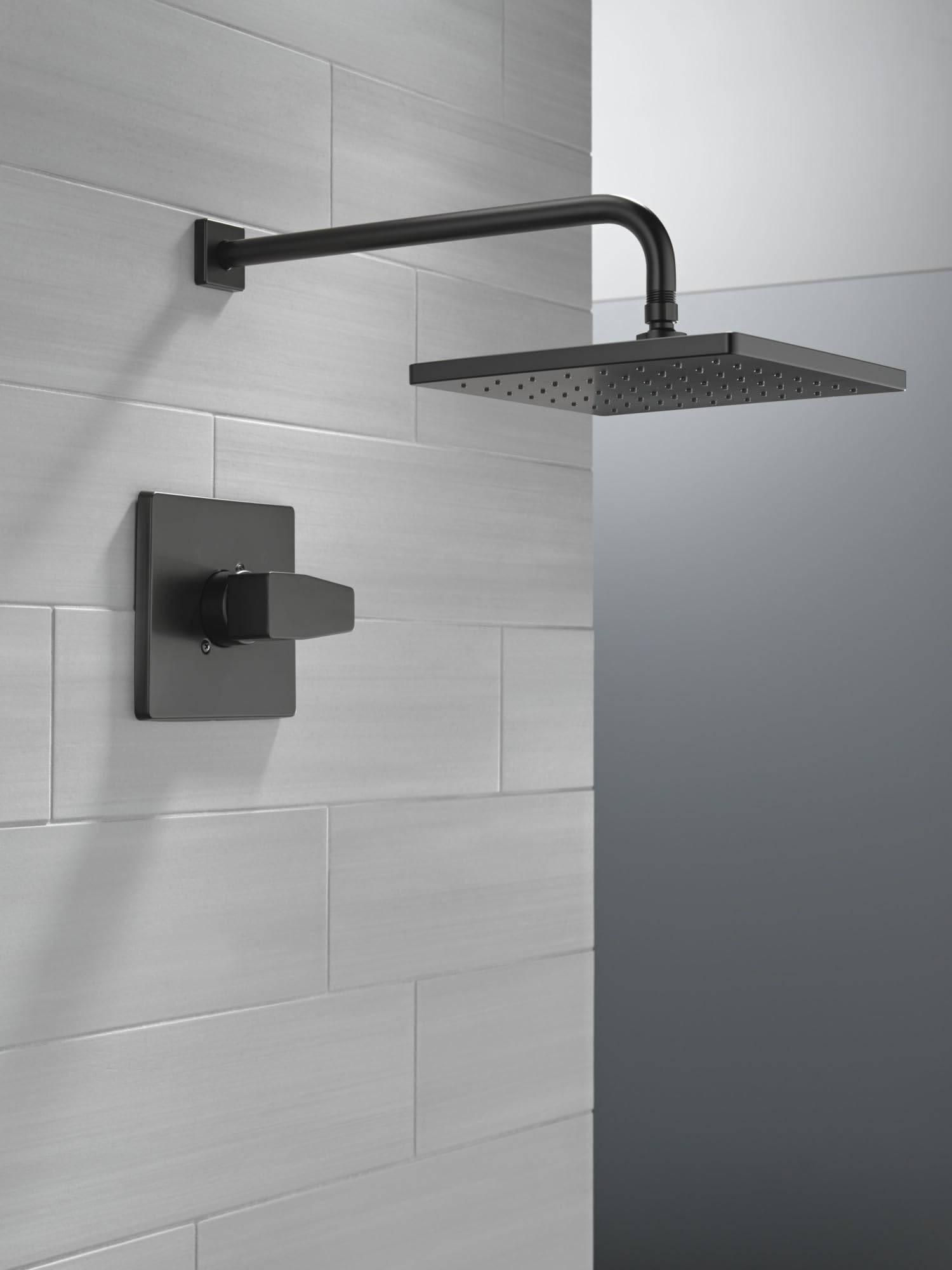 Matte black shower trim with square wall-mounted control valve and rectangular overhead showerhead on tiled bathroom wall.