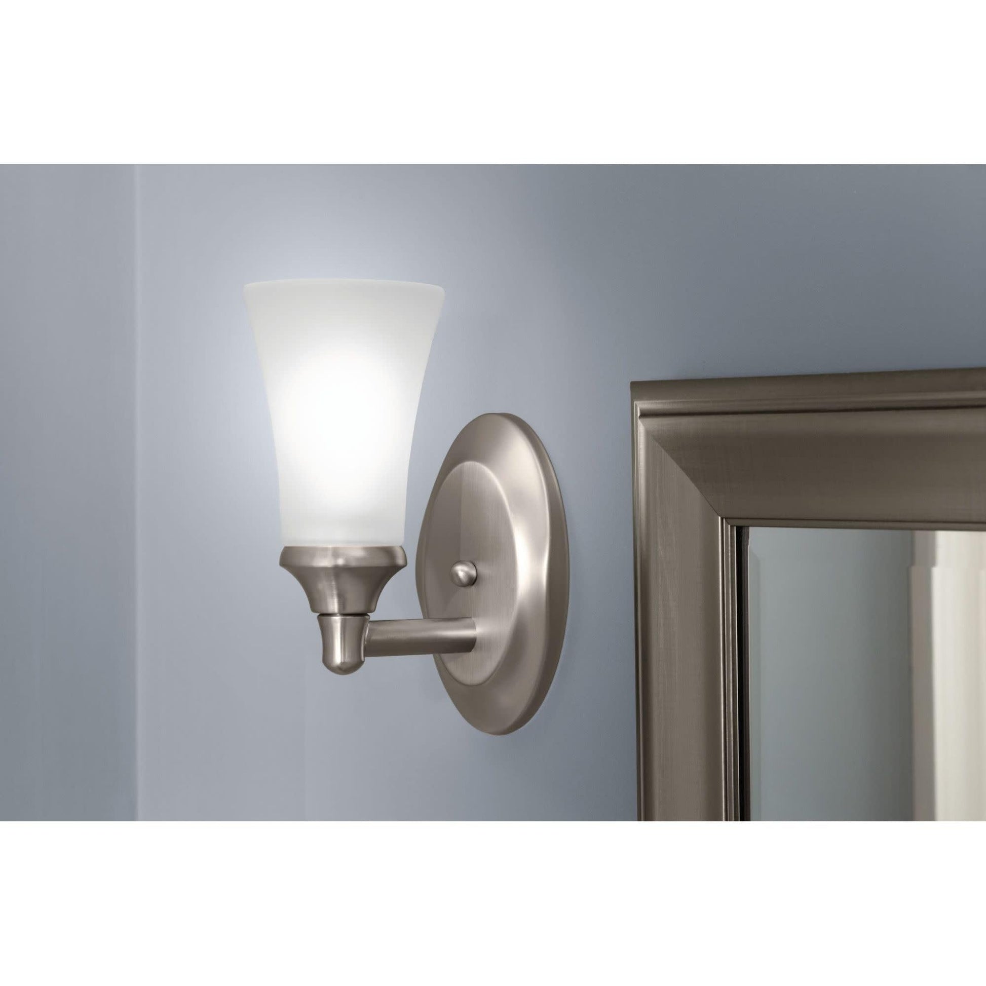 Oil-rubbed bronze bathroom vanity light with frosted glass shade mounted on wall next to mirror.