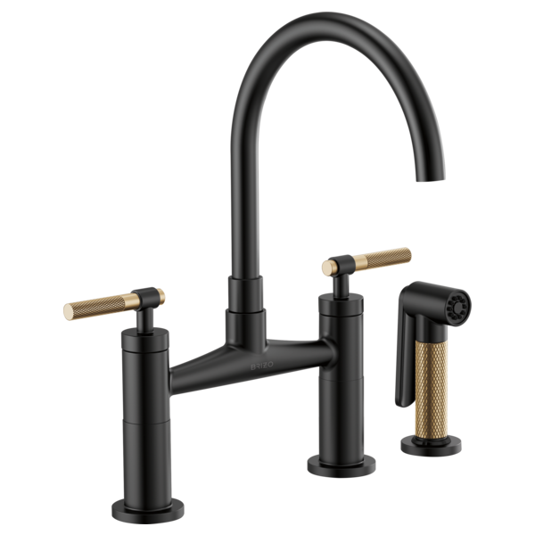 Black bridge faucet with curved arc spout, two knurled gold handles, and matching side spray attachment.