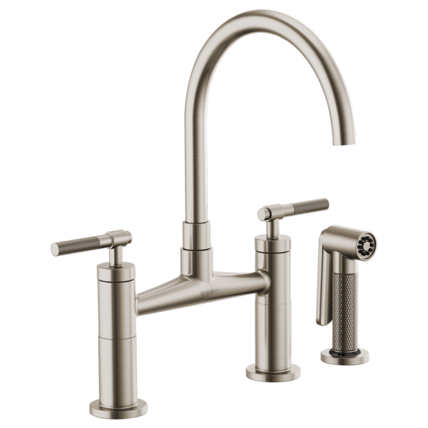 Brushed nickel bridge faucet with curved arc spout, dual knurled handles, and side spray attachment.