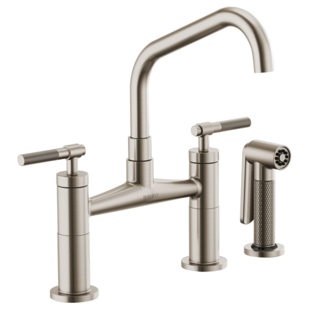 Stainless steel bridge faucet with angled spout, two knurled handles, and matching side sprayer.