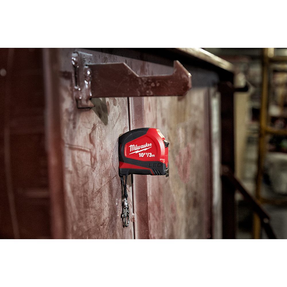 Red and black Milwaukee keychain tape measure with 10ft/3m capacity and metal attachment ring hanging from a hook.