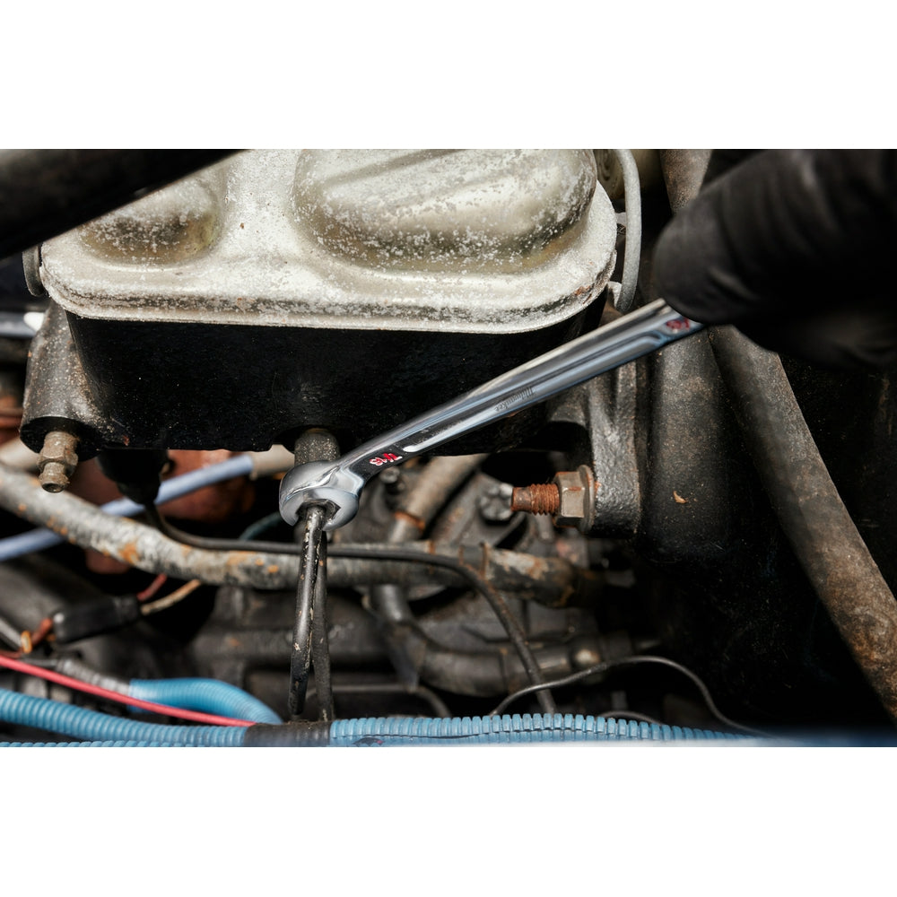 Chrome double-end flare nut wrench with red branding, positioned on engine fuel line fitting during use.