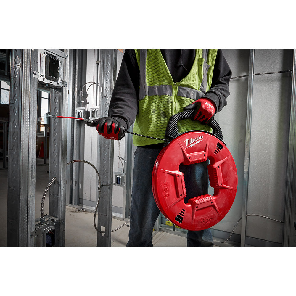 Worker in safety vest holding red Milwaukee fish tape reel with black polyester line being fed into metal conduit.
