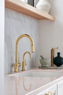 Polished gold widespread bathroom faucet with high arc spout and two handles above white sink.