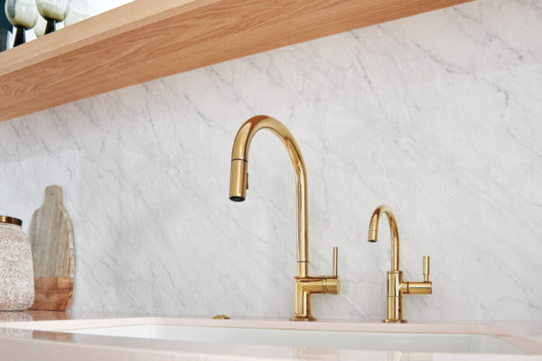 Polished gold widespread bathroom faucet with high arc spout and two handle controls mounted on marble countertop.