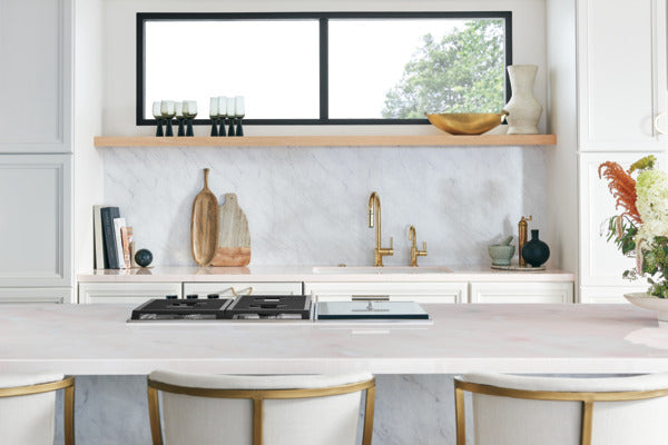 Polished gold widespread bathroom faucet with high arc spout installed on marble backsplash in modern kitchen.