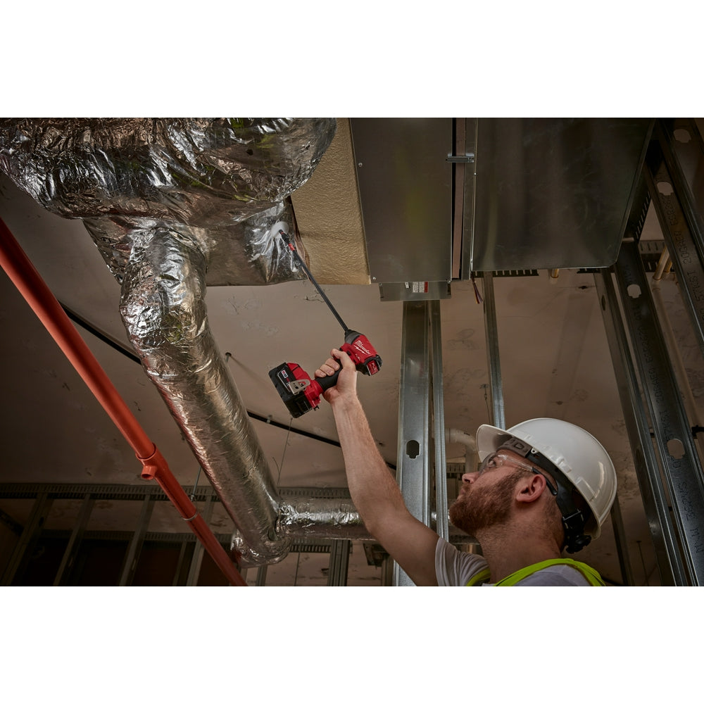 Worker in white hard hat holding red and black Milwaukee impact driver with bit holder while working on ductwork.