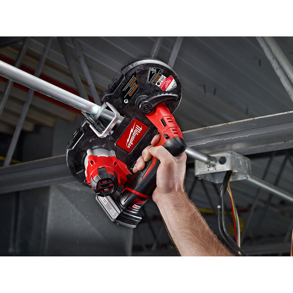 Red and black cordless band saw held in hand cutting through metal material.