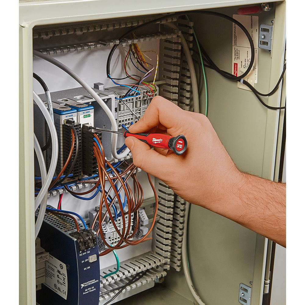 Red and black Milwaukee precision screwdriver with circular handle being used in electrical panel with wires and components.