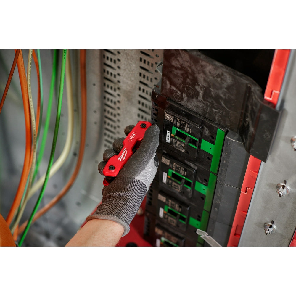Red folding hex key set held in a gloved hand near electrical equipment.