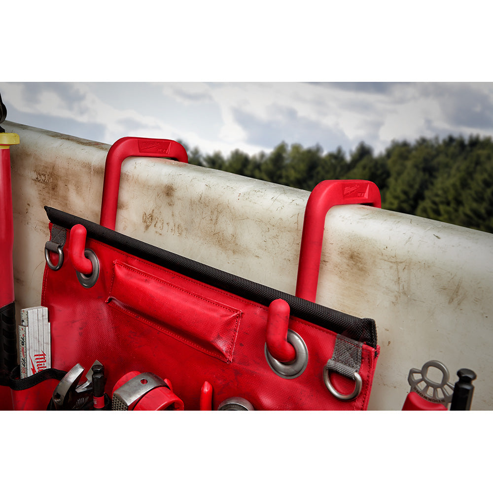 Red bucket hook with metal D-ring attached to red tool bag hooked over white cylindrical bucket rim.