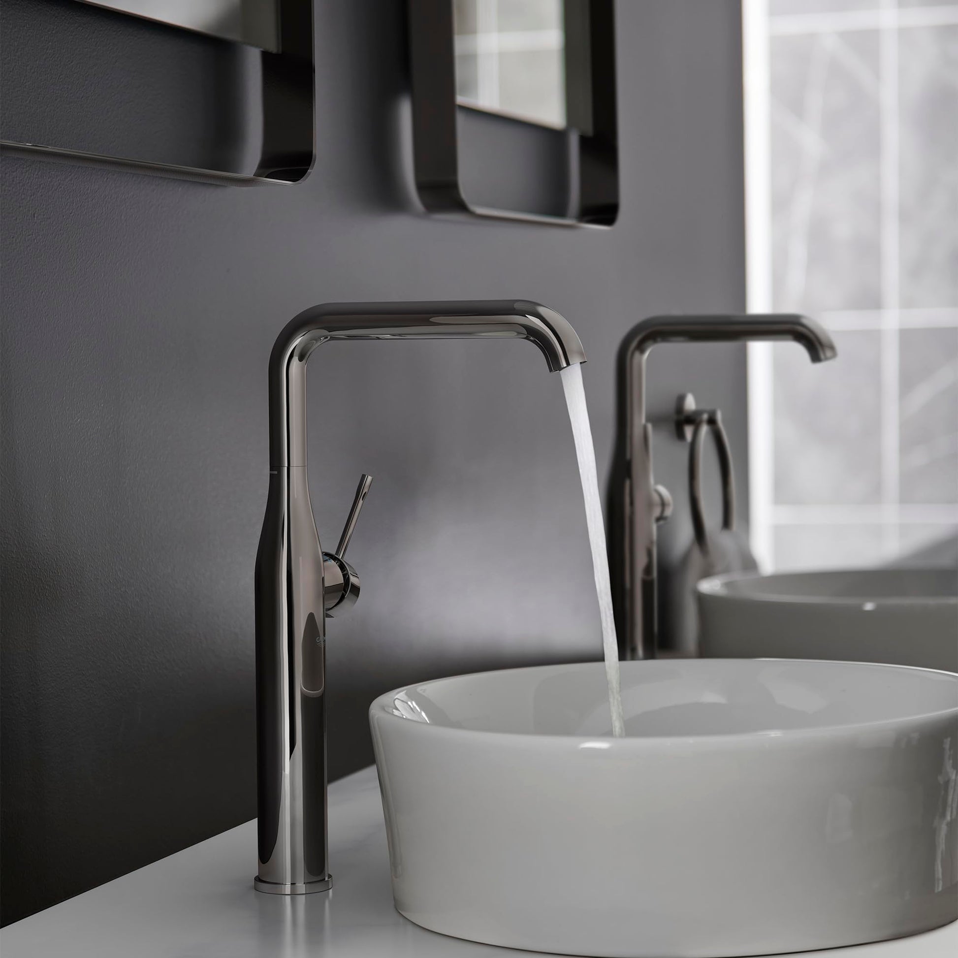 Grohe Essence single-handle faucet in hard graphite with tall curved spout dispensing water into white vessel sink.