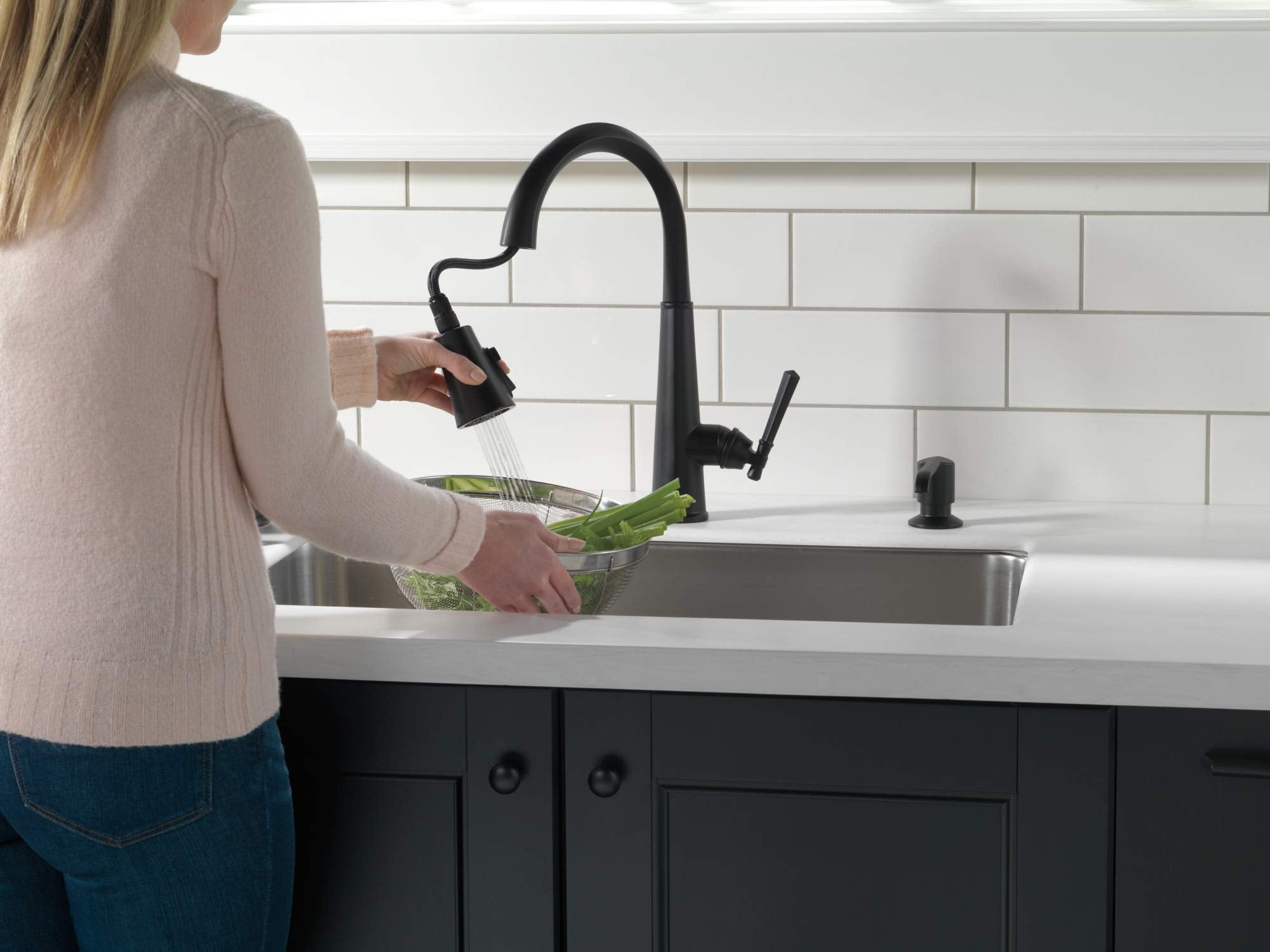 Matte black metal soap dispenser pump mounted on kitchen countertop next to faucet.