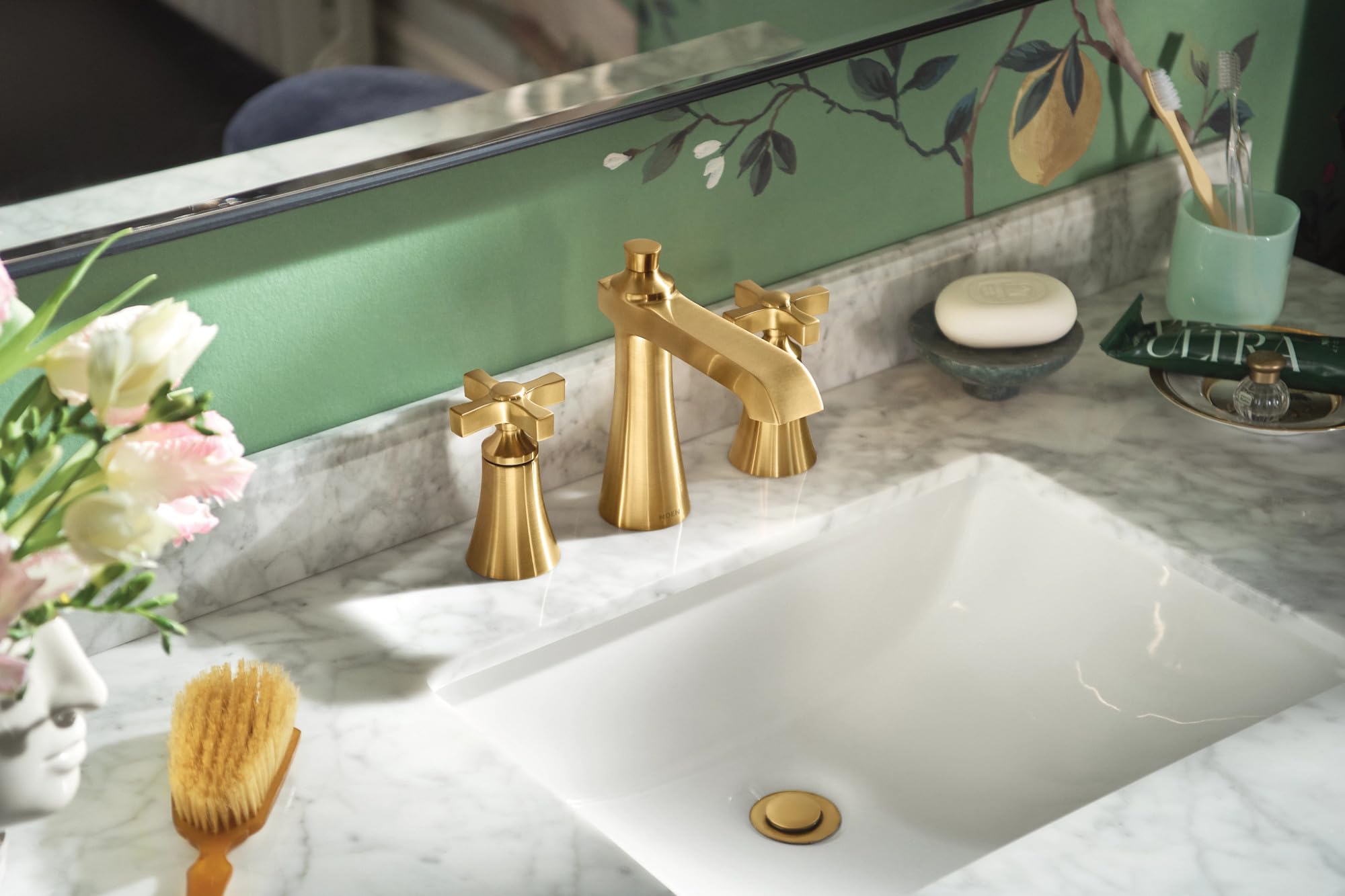 Brushed gold two-handle bathroom faucet with cross handles installed on marble countertop above white sink.