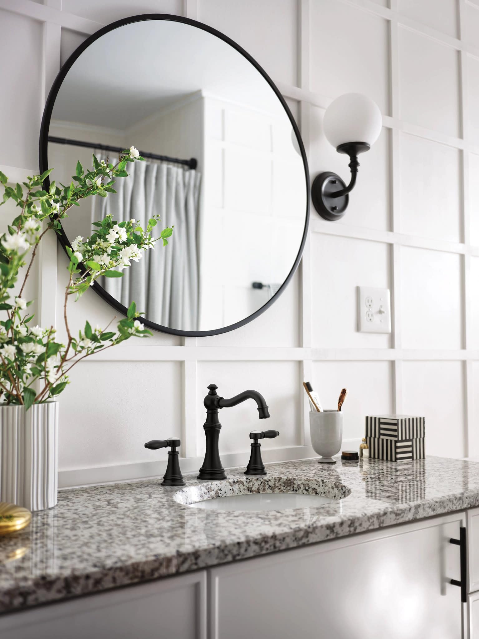 Matte black two-handle lever bathroom faucet with curved spout installed on gray granite countertop.