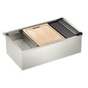 Stainless steel undermount sink with wooden cutting board, black drying rack, colander, and grid accessories displayed.