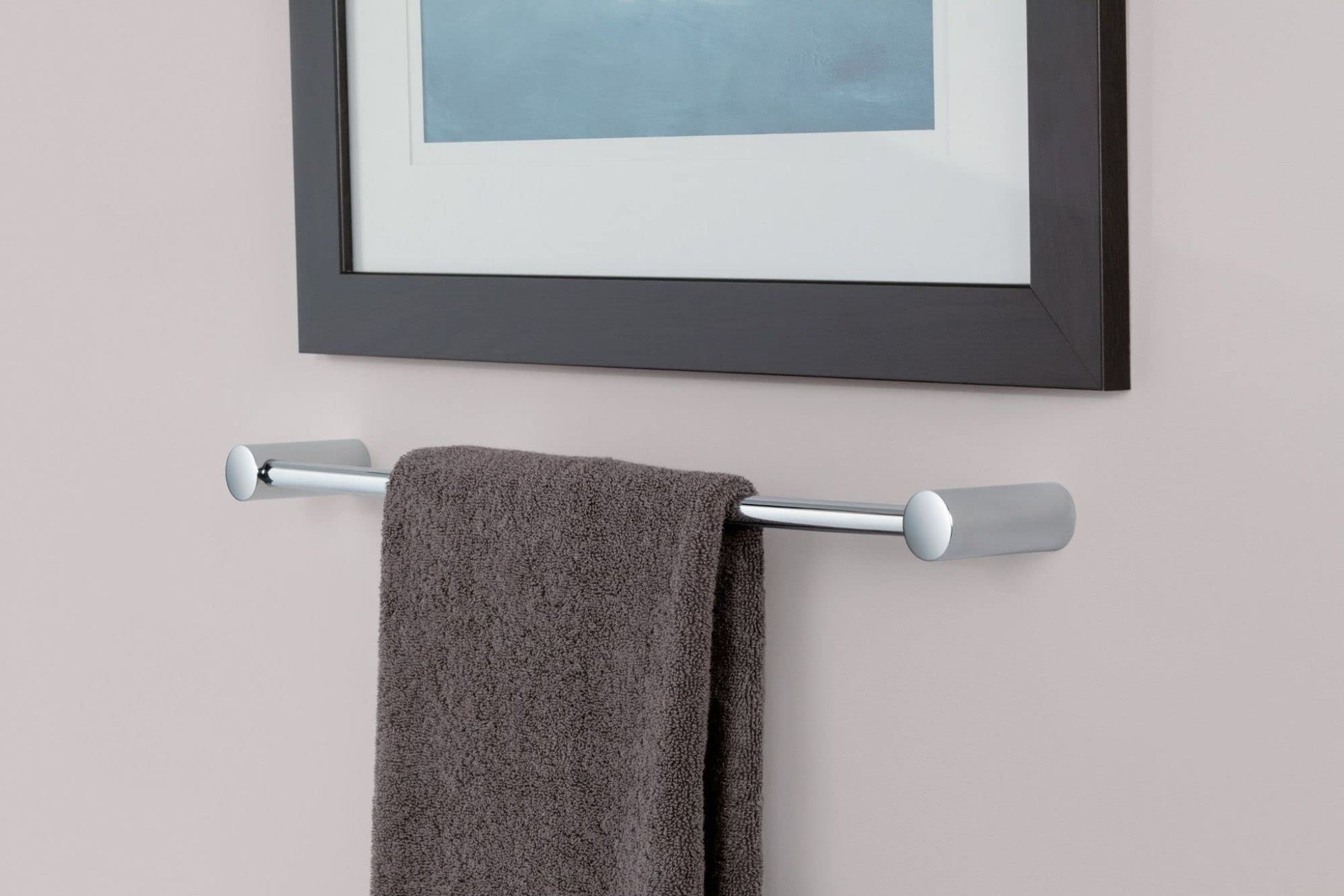 Chrome wall-mounted towel bar with cylindrical end caps holding a folded gray towel against a light wall.