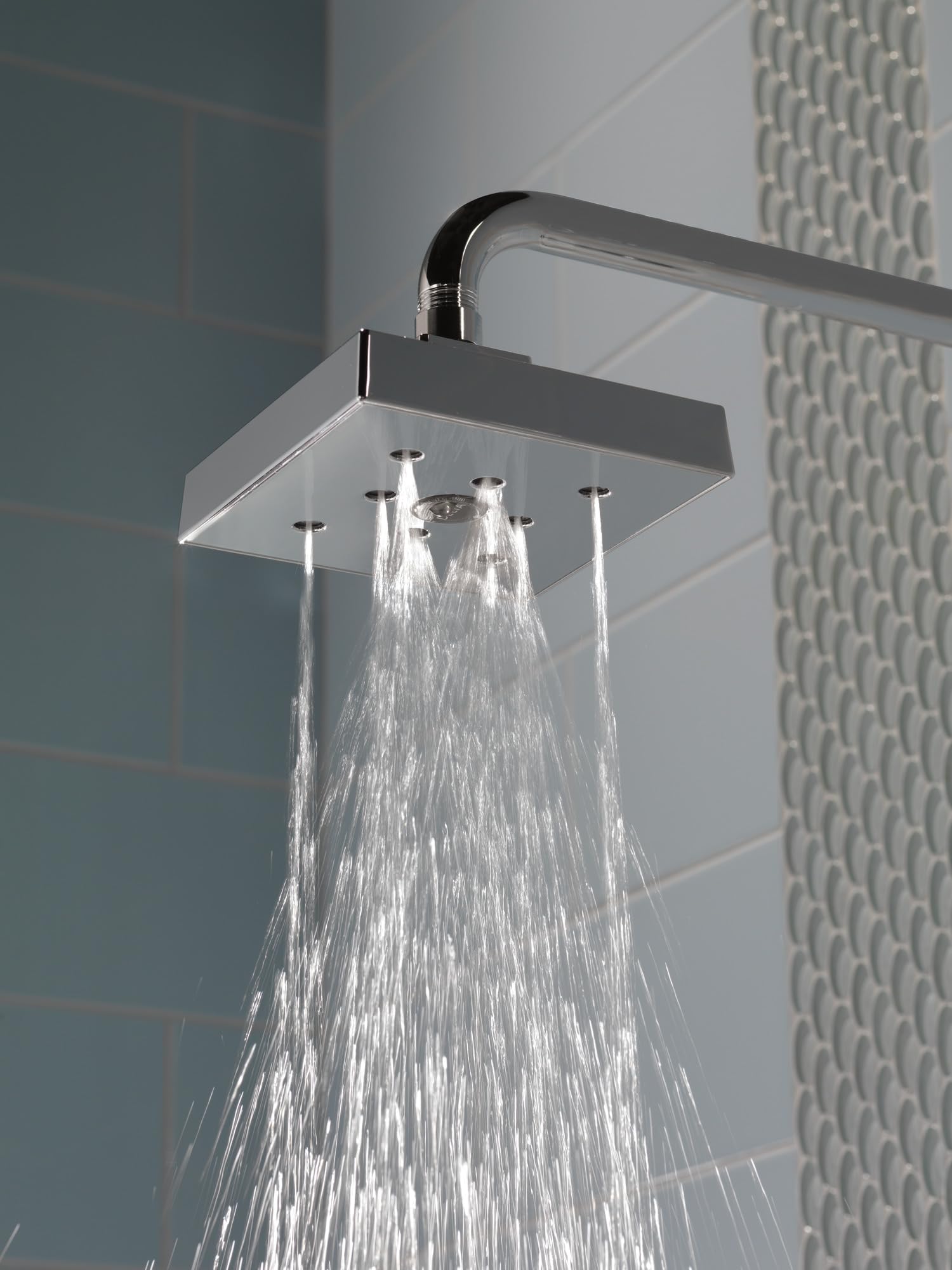 Black stainless steel square shower head with curved arm connection and multiple water jets flowing downward.