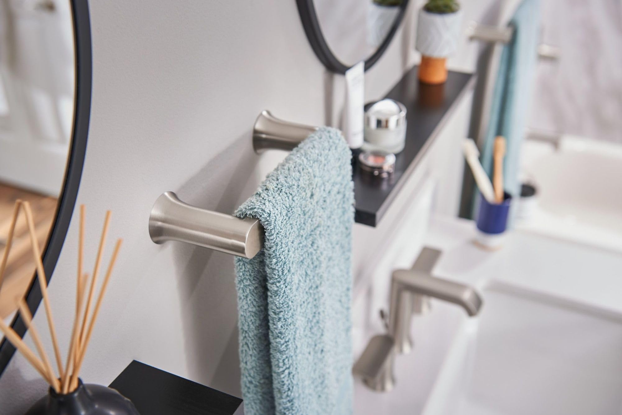 Brushed nickel hand towel bar mounted on white bathroom wall with light blue towel draped over it.