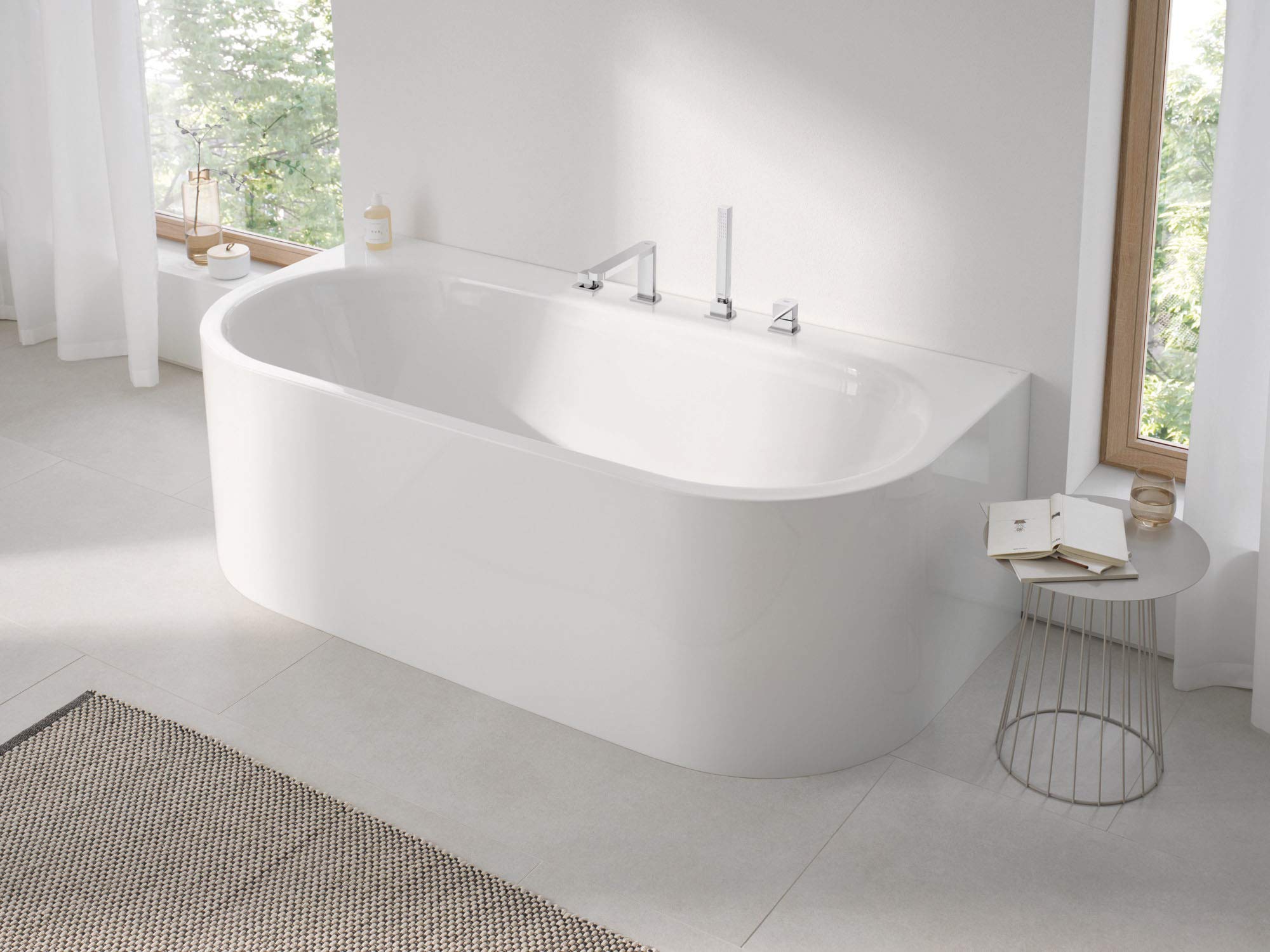 Chrome roman tub faucet with single handle and hand shower mounted on white freestanding bathtub.