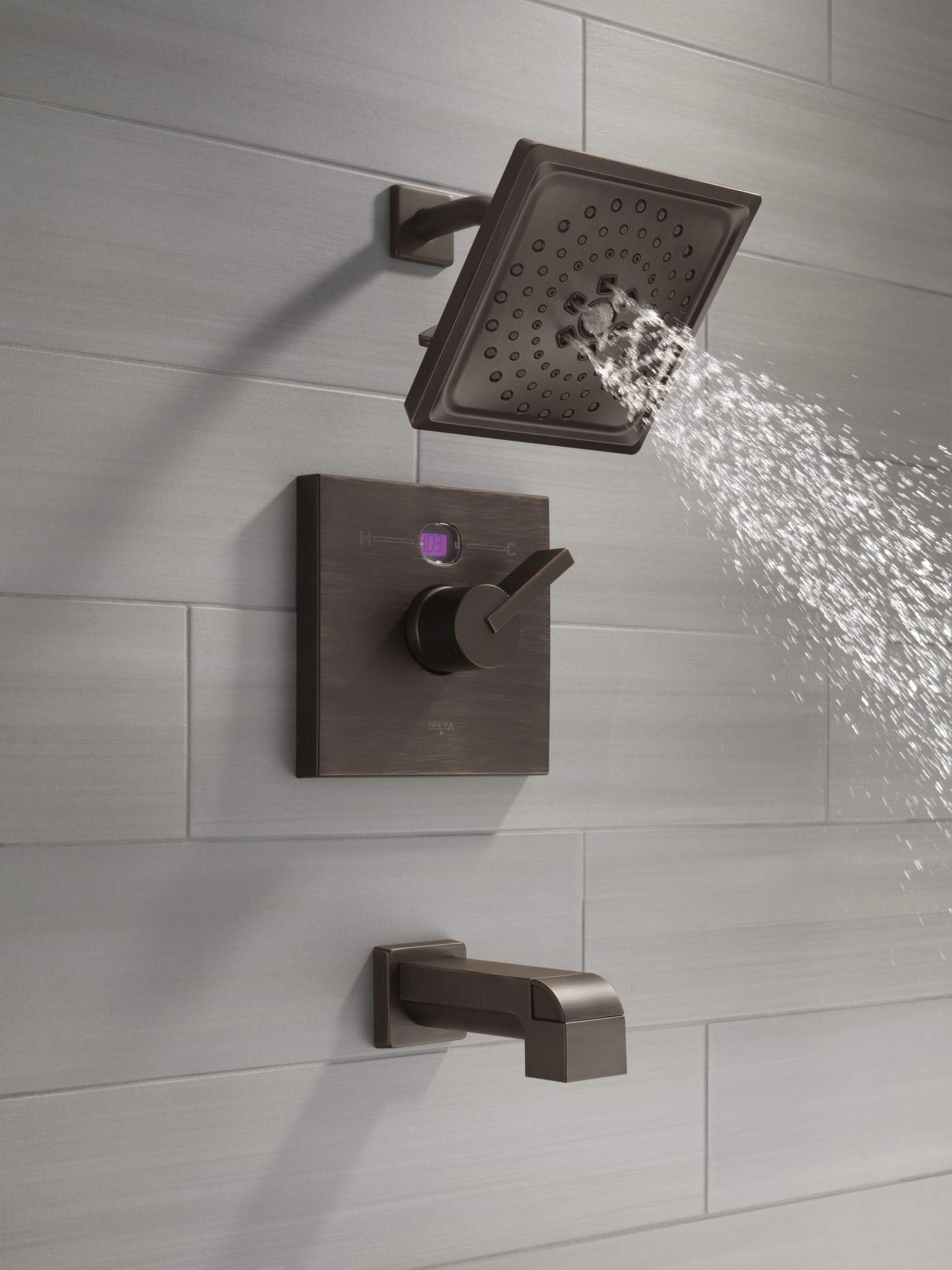 Champagne bronze tub spout with pull-up diverter mounted on tile wall below rainfall showerhead.