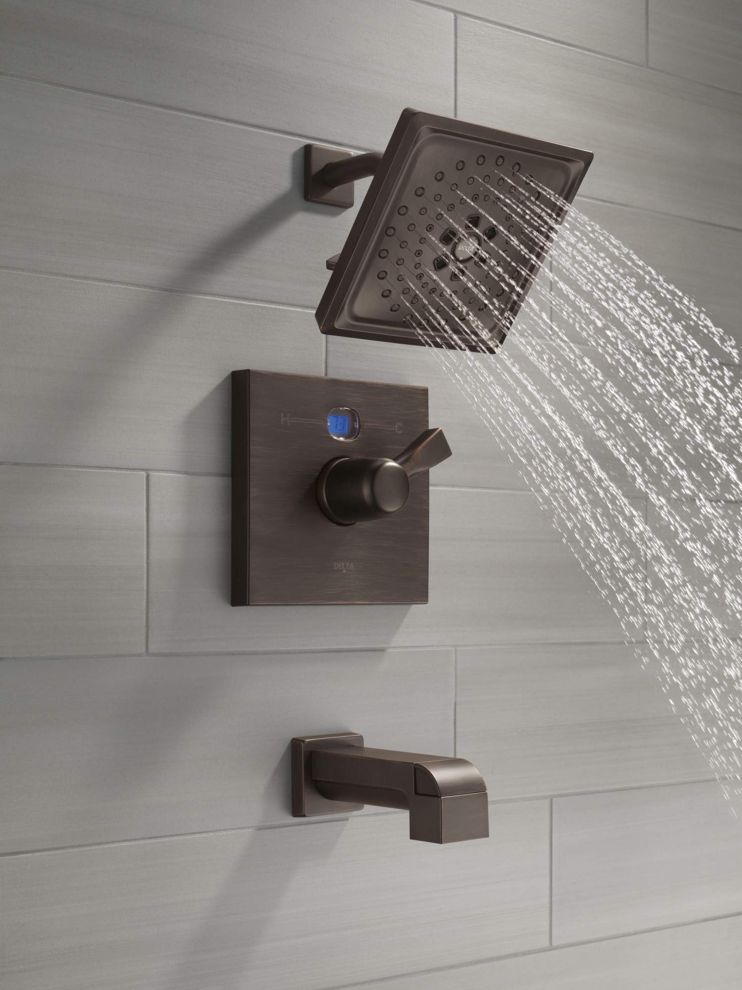 Champagne bronze tub spout with pull-up diverter mounted on white subway tile wall with matching showerhead and valve trim.