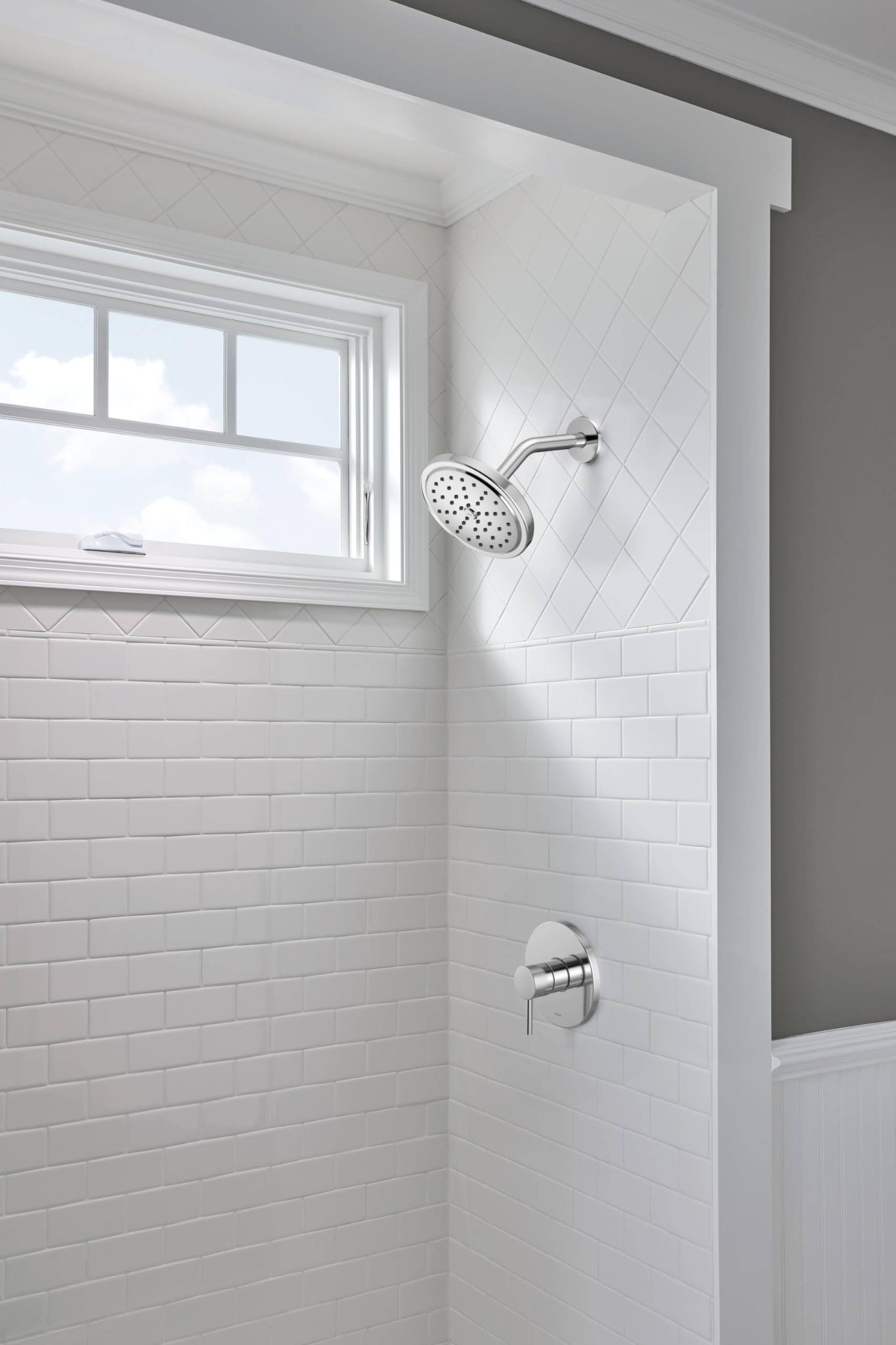 Chrome shower trim kit with control handle and showerhead mounted on white subway tile shower wall.