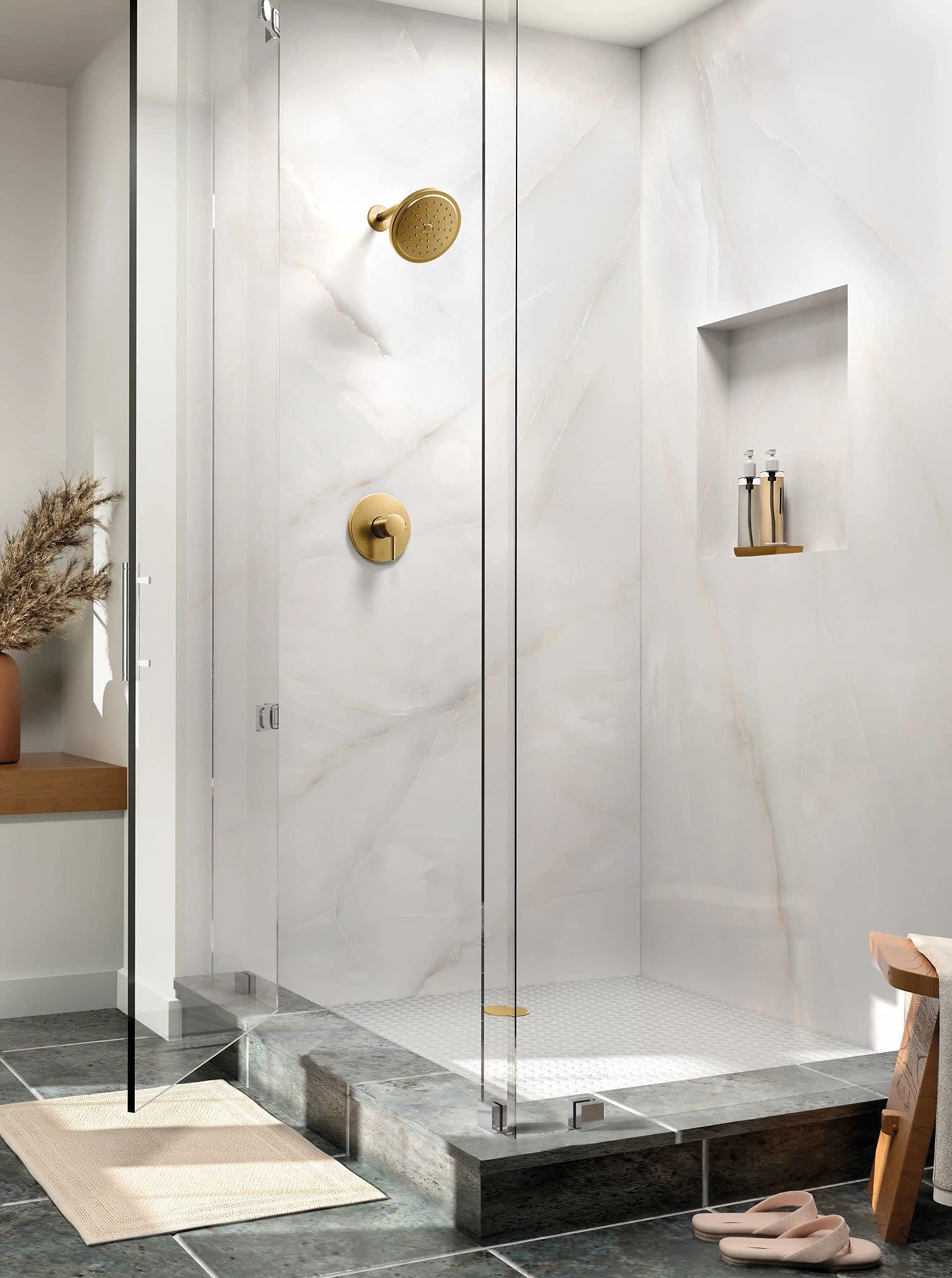 Brushed gold shower trim kit with round showerhead and valve handle mounted on white marble tile wall.