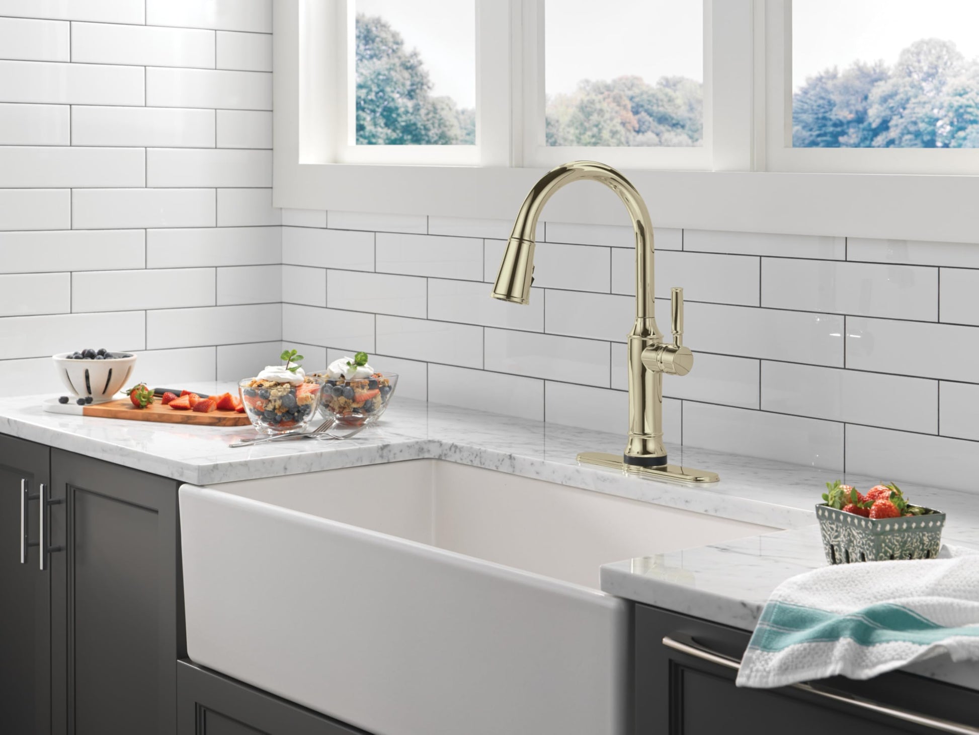 Gold pulldown kitchen faucet with high arc spout mounted above white farmhouse sink.