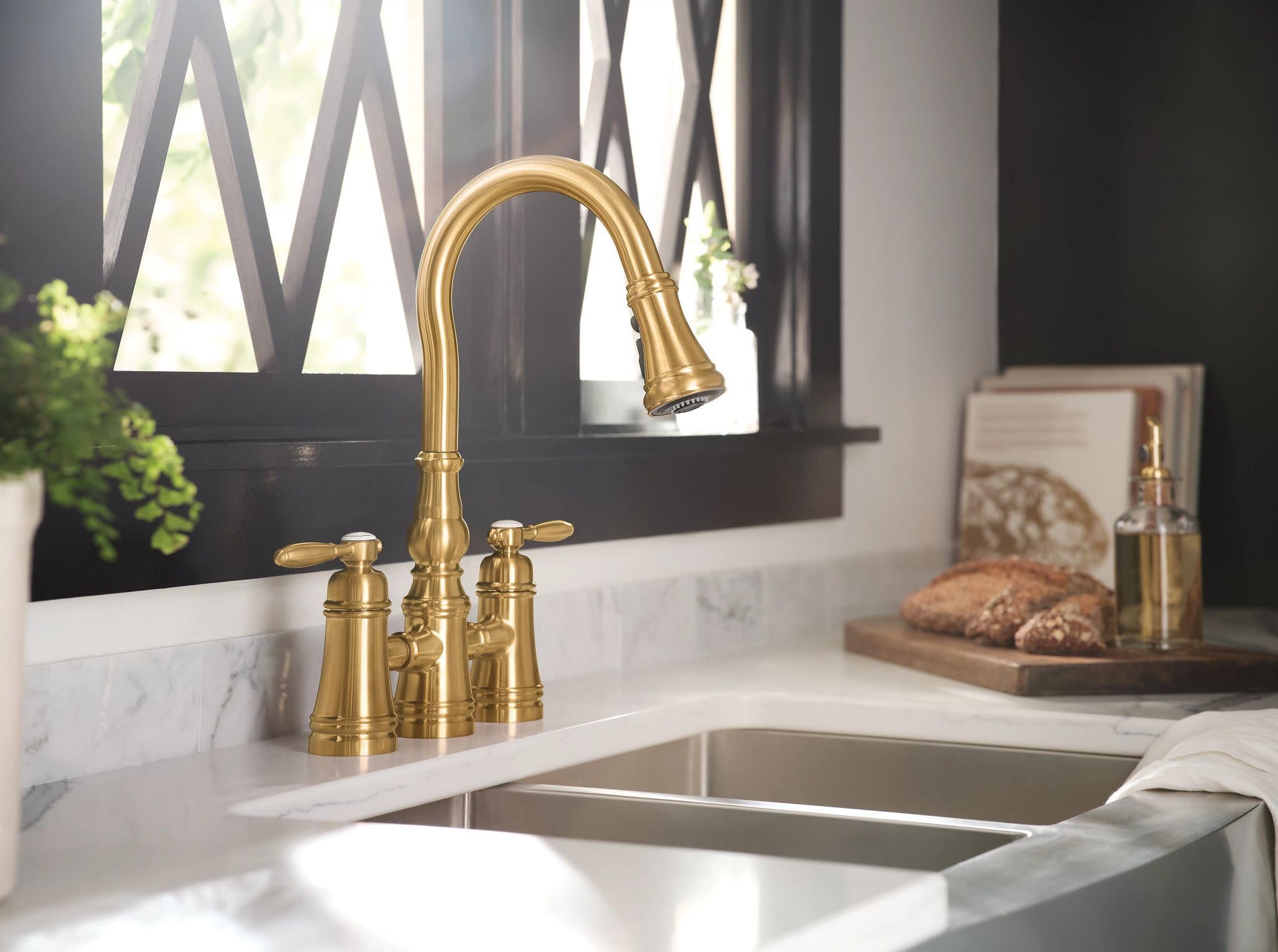 Brushed gold two-handle bridge kitchen faucet with pulldown spout installed above a double basin sink.