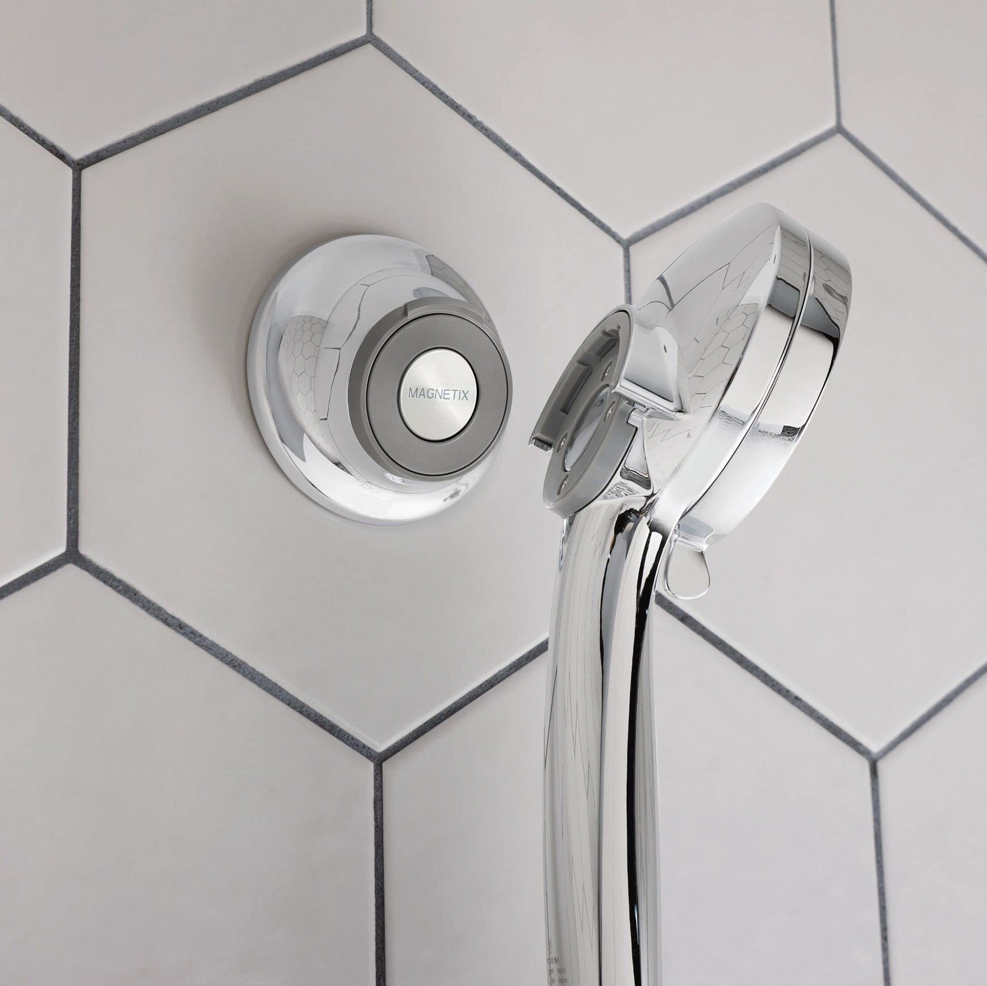 Chrome and white magnetic cradle mounted on tile wall holding showerhead with attached hose.