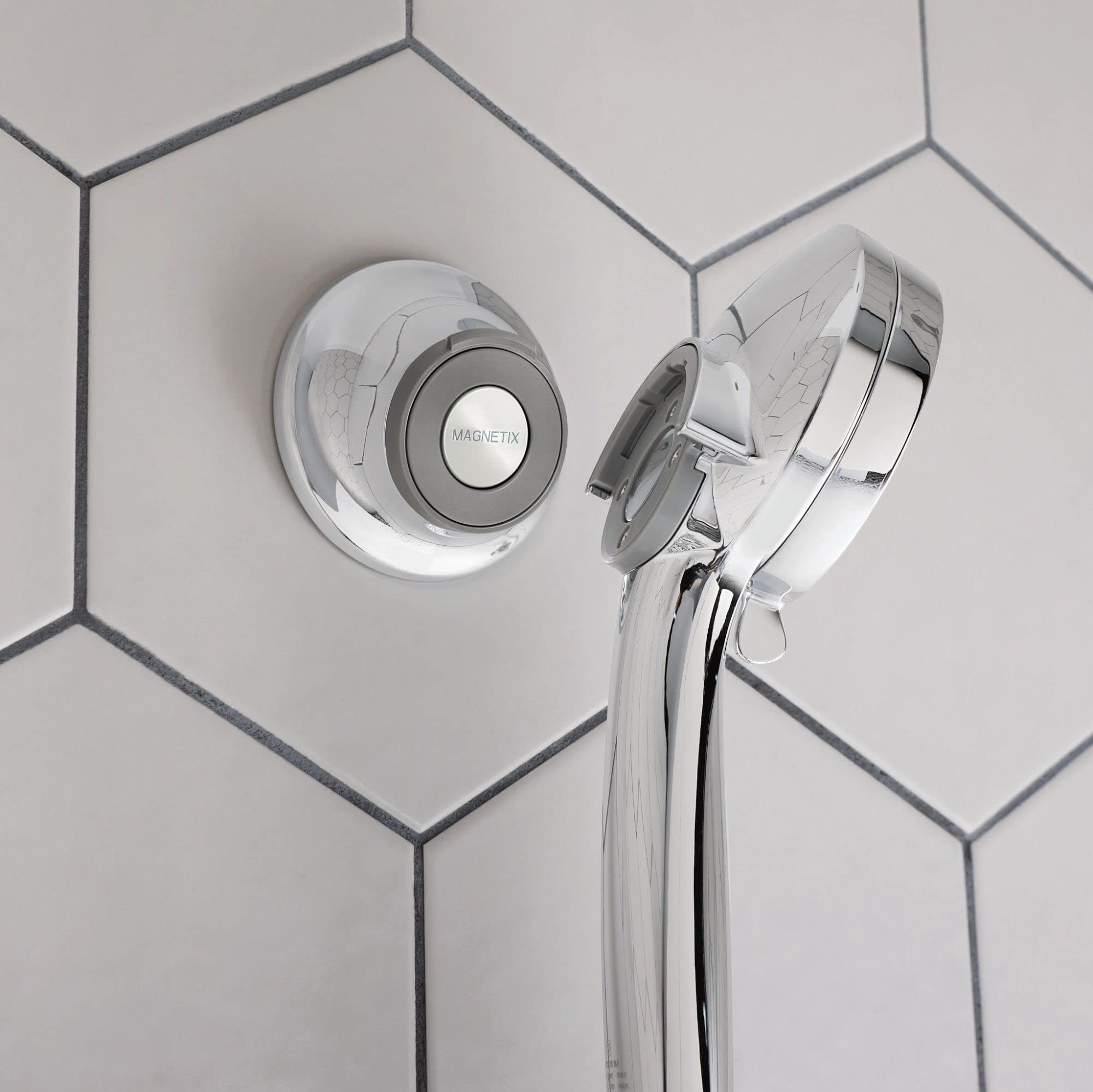 Chrome and white magnetic cradle mounted on tile wall holding showerhead with attached hose.
