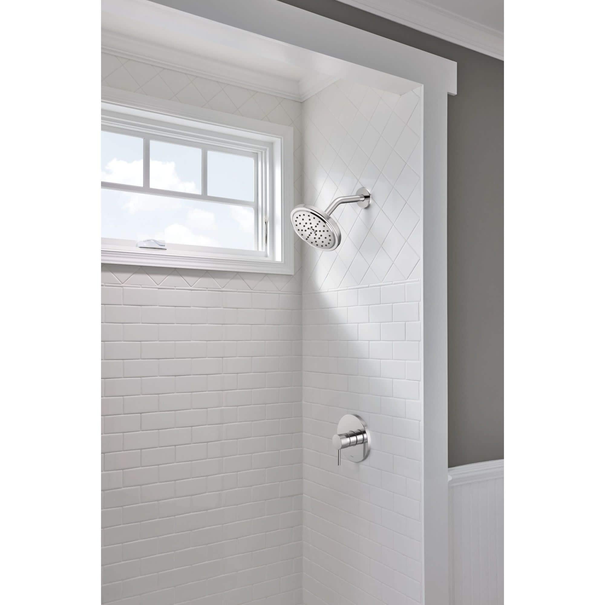 Brushed nickel shower trim with single handle control, round showerhead, and wall-mounted valve on white subway tile.