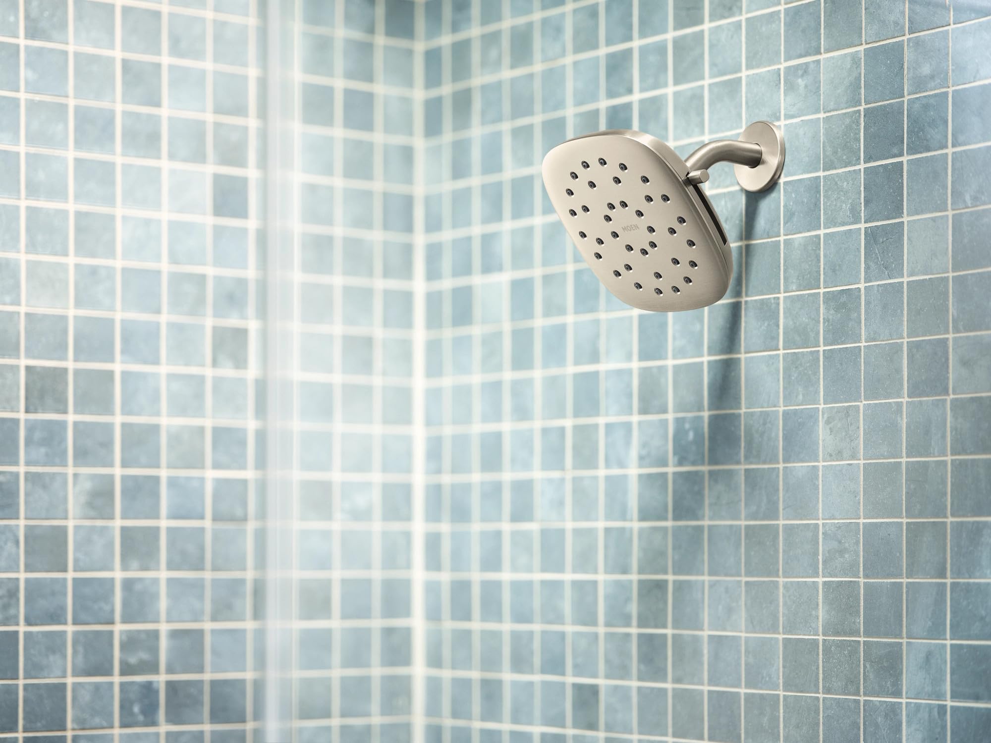 Square brushed nickel rain shower head with multiple spray holes mounted on tile shower wall.